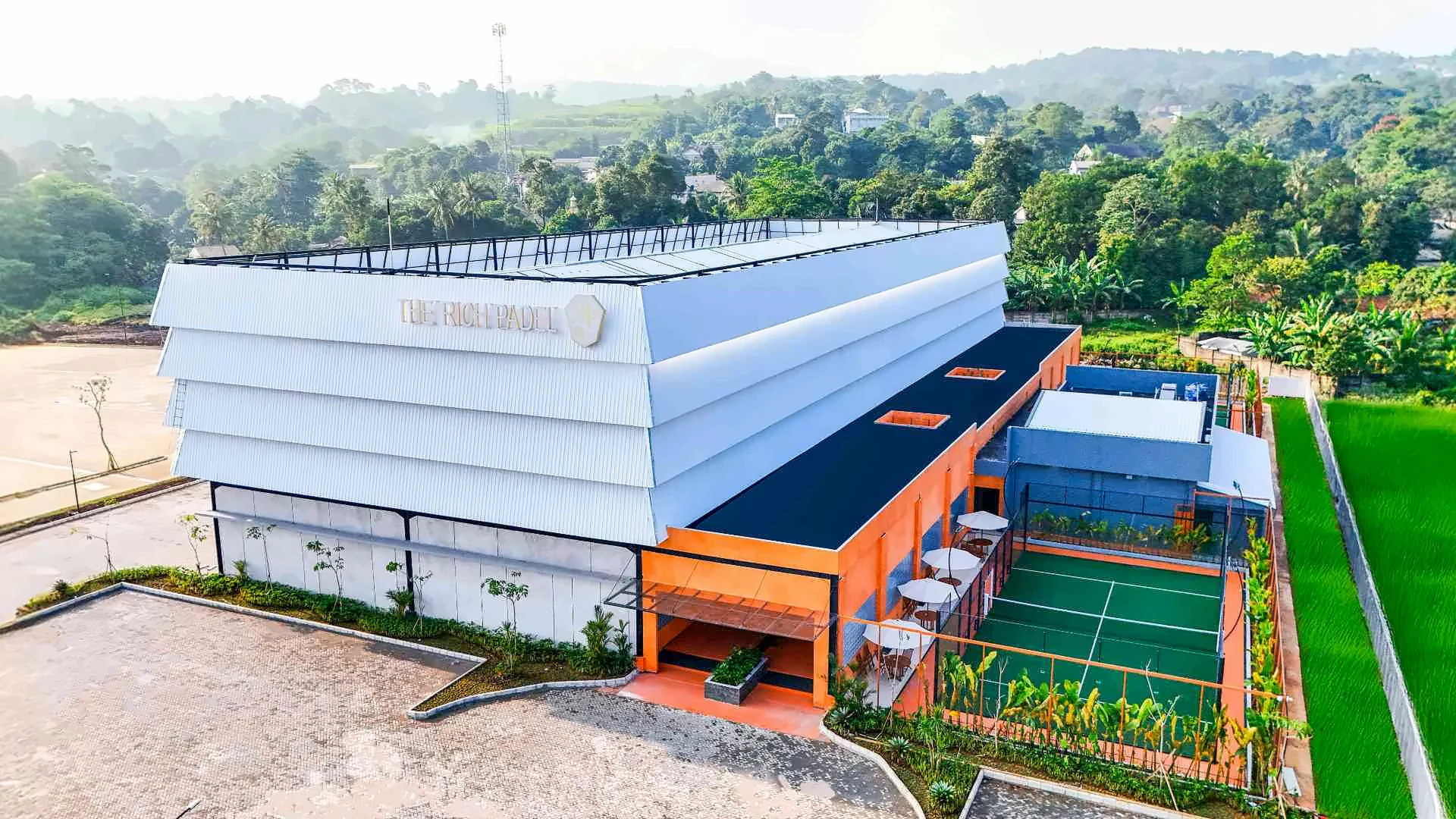 Aerial view of The Rich Padel building at Xforia Sentul, its outdoor court beside it and the Sentul hills behind