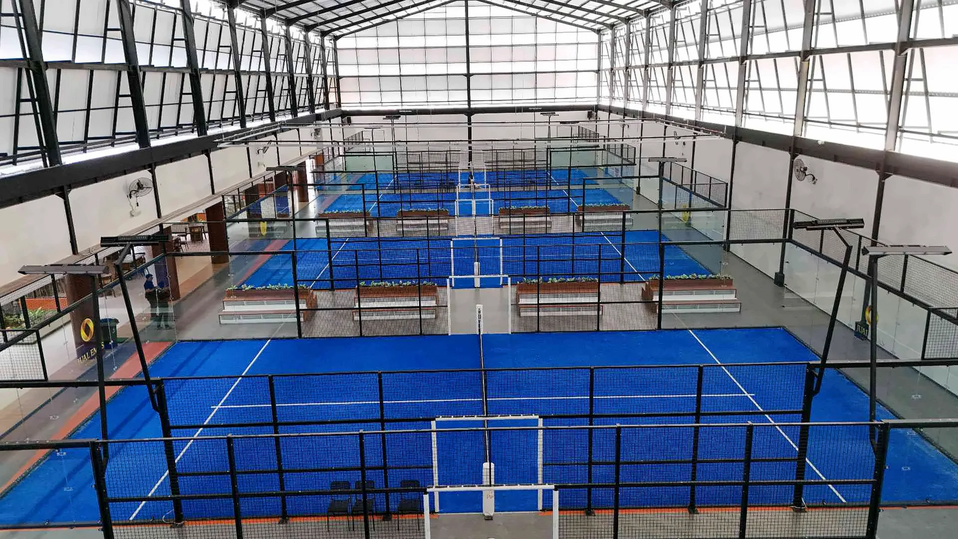 The indoor hall seen from above: blue courts in a row under a high steel and polycarbonate roof