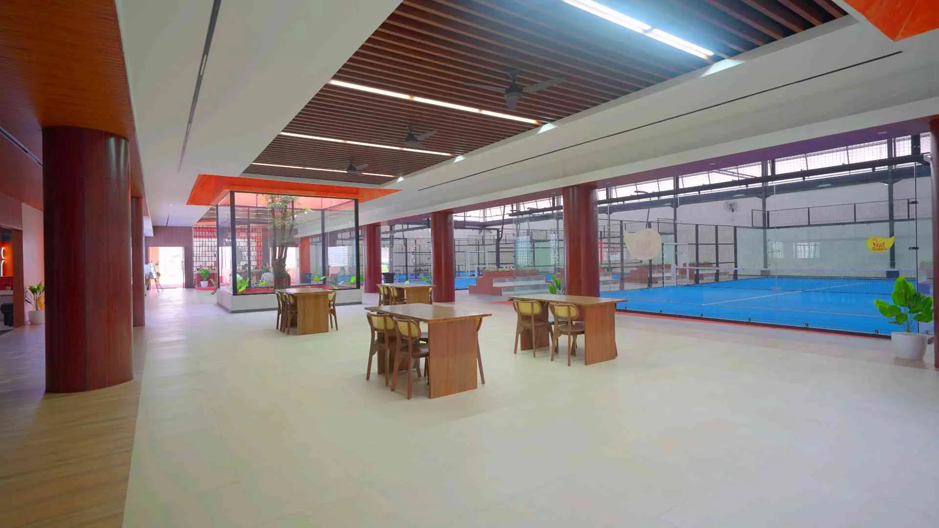 Meetground lounge with timber tables and chairs, the blue courts beyond the glass