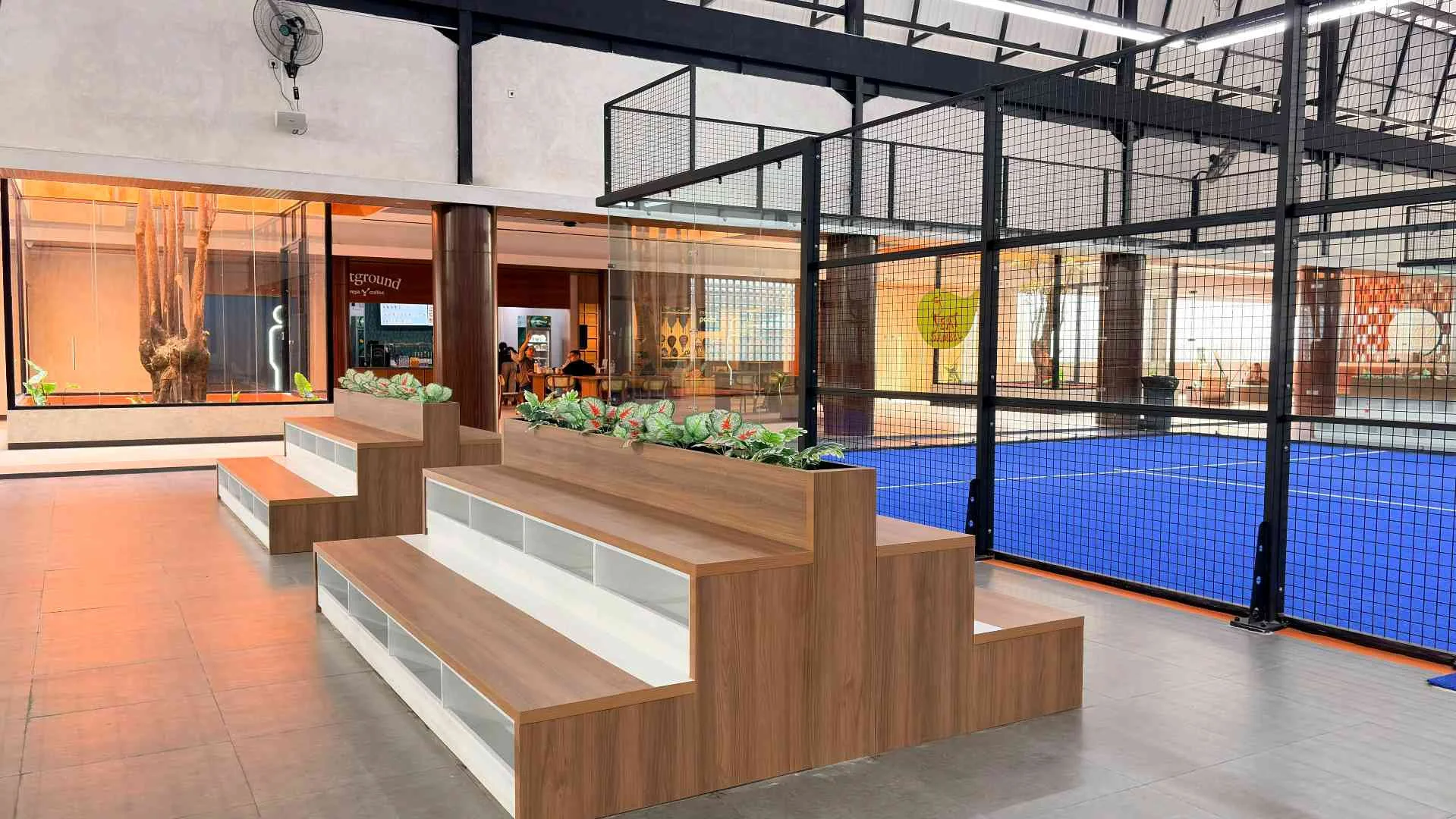Timber tiered seating and planters beside the blue indoor courts